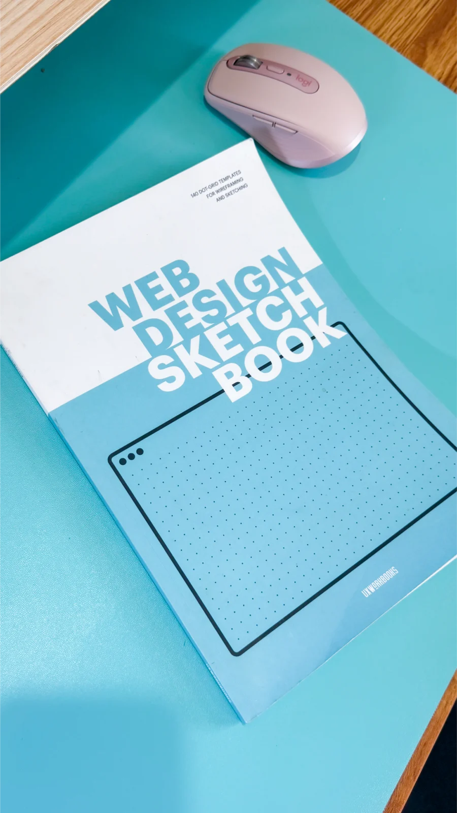 Web design sketchbook with dot grid templates used for website wireframing and project planning, placed next to a pink wireless mouse on a teal desk.

